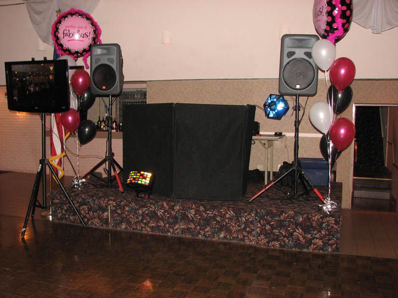 DJ setup with speakers, screen, and balloons at an event.