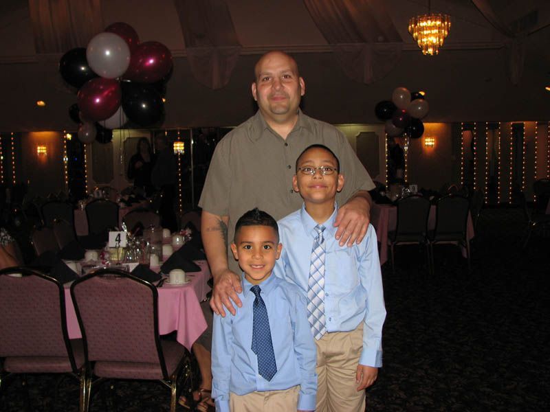 Man with two boys posing at a formal event, balloons in background.