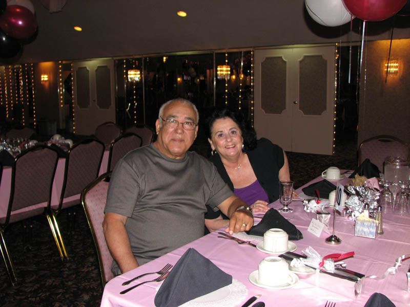 Couple seated at a pink table in a decorated room, smiling.