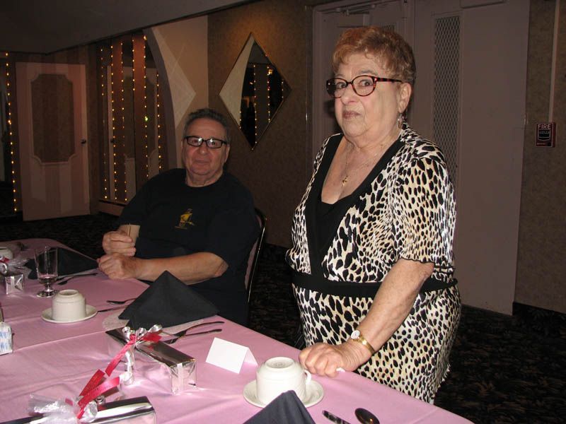 A woman in a leopard-print dress and a man with glasses sit at a table set for dinner.