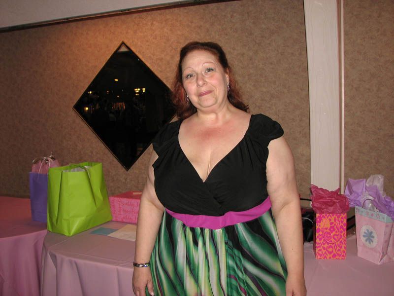 Woman in a black and green dress at a table with gifts; neutral expression.