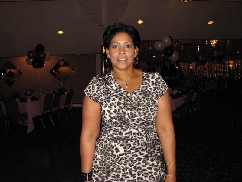 Woman in a leopard-print dress stands in a dimly lit banquet hall, decorated for an event.
