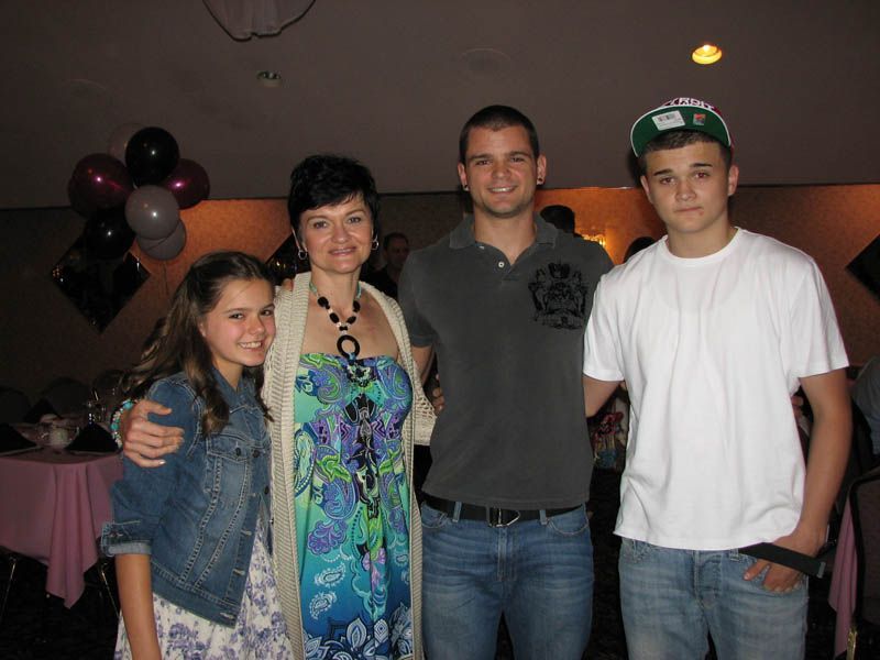 Family posing together at a party, inside. Woman in blue dress, teen in a cap, girl in denim jacket, man in grey polo.