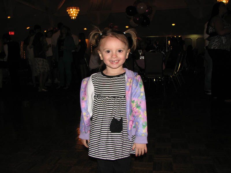 Girl with pigtails smiles, wearing a striped dress and floral cardigan, indoors.
