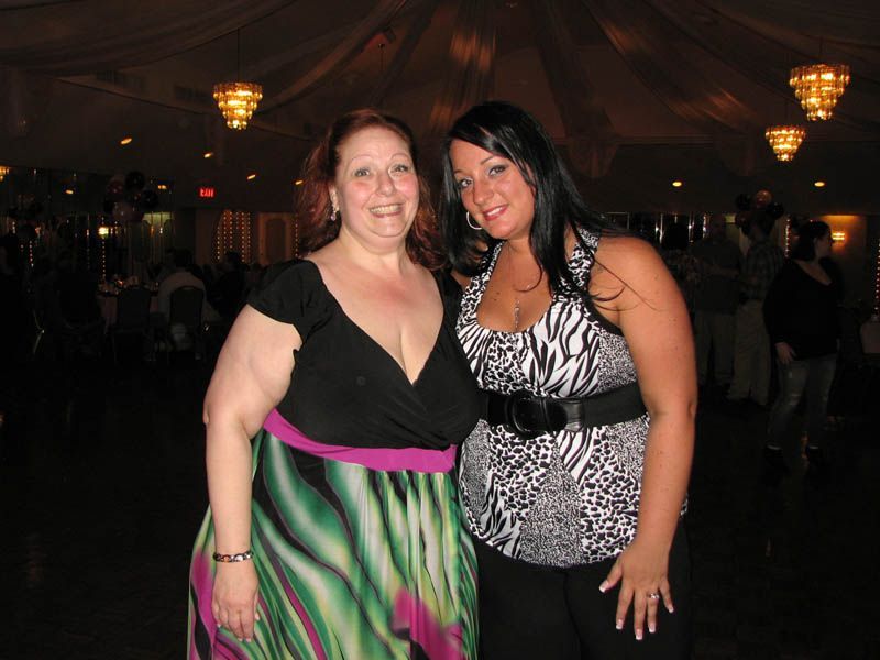 Two women pose at an indoor event; one in zebra print top, one in black and colorful dress.