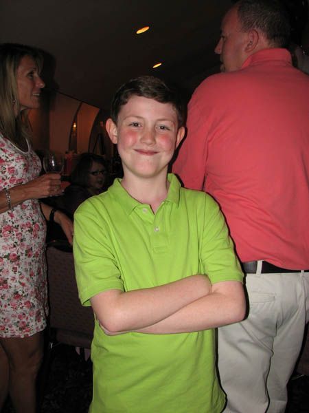 Boy in green polo shirt with arms crossed, smiling. People in background.