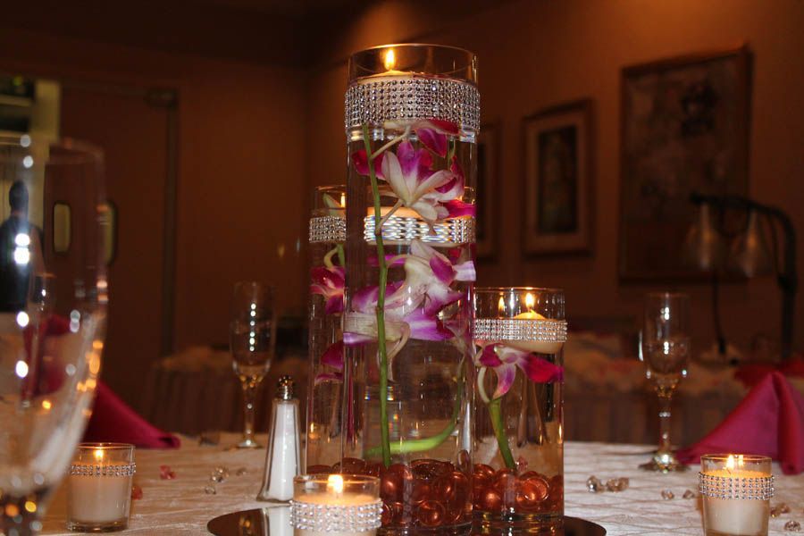 Elegant floral centerpiece with orchids in water-filled vases on a wedding table with candles.