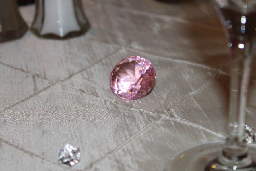 Pink gemstone on a cream-colored, textured tablecloth with wine glass and salt shakers.