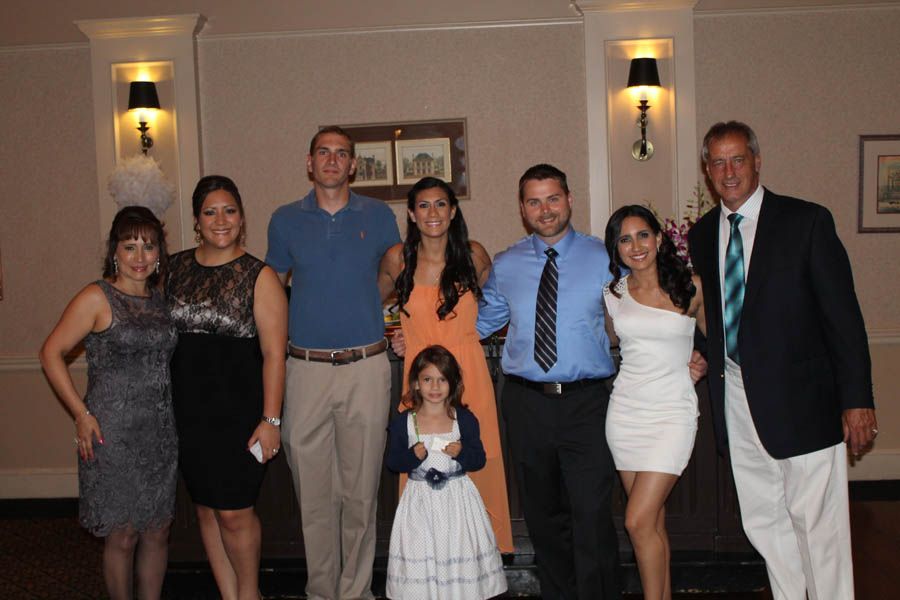Group of people posing for a photo indoors, in front of a wall with sconces, wearing formal attire.