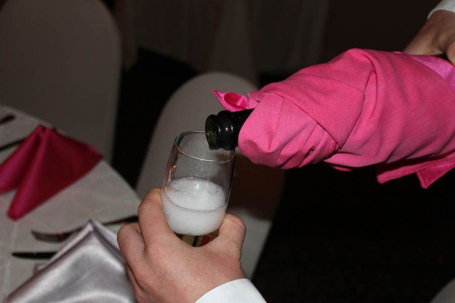 Champagne being poured into a glass, bottle wrapped in pink fabric.