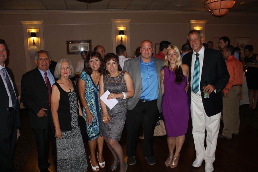 Group of people at an indoor event, posing for a photo. Men in suits, some in bright colors.