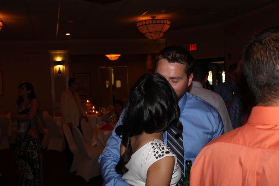 Couple kissing at a wedding reception; man in blue shirt, woman in white dress, surrounded by guests.