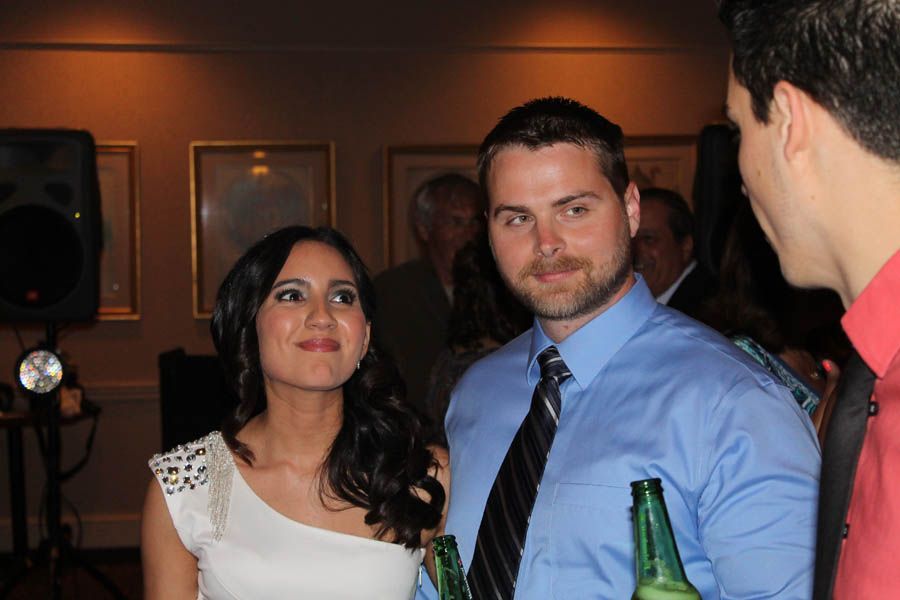 Woman in white dress and man in blue shirt and tie at an event, smiling, with another man looking on.