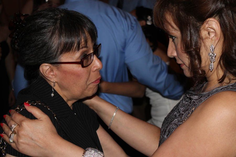 Woman in glasses being embraced by another woman; both in formal attire, possibly at an event.