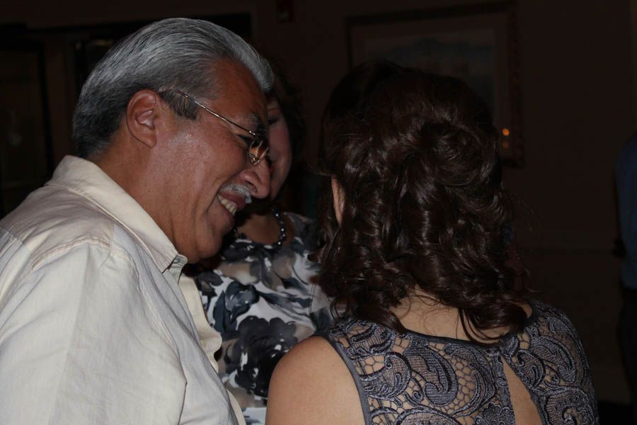 Man laughs while talking to a woman with curly hair; indoor setting with other people present.