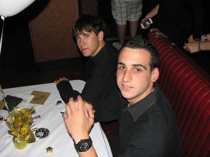 Two men at a table, both wearing black shirts. One looks at the camera.