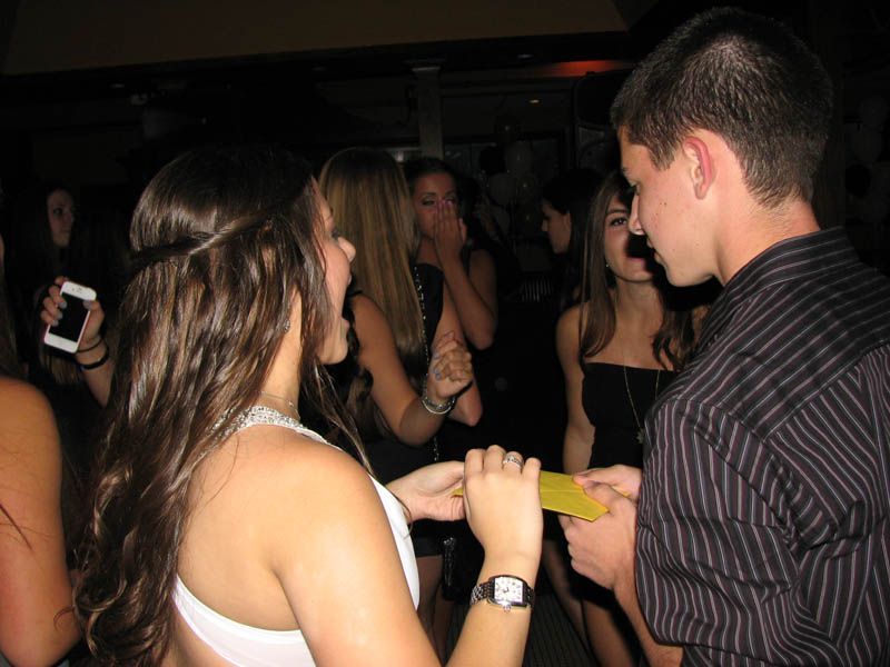 Young people in a dimly lit club. A woman and a man are holding a yellow item, possibly a receipt, talking to each other.