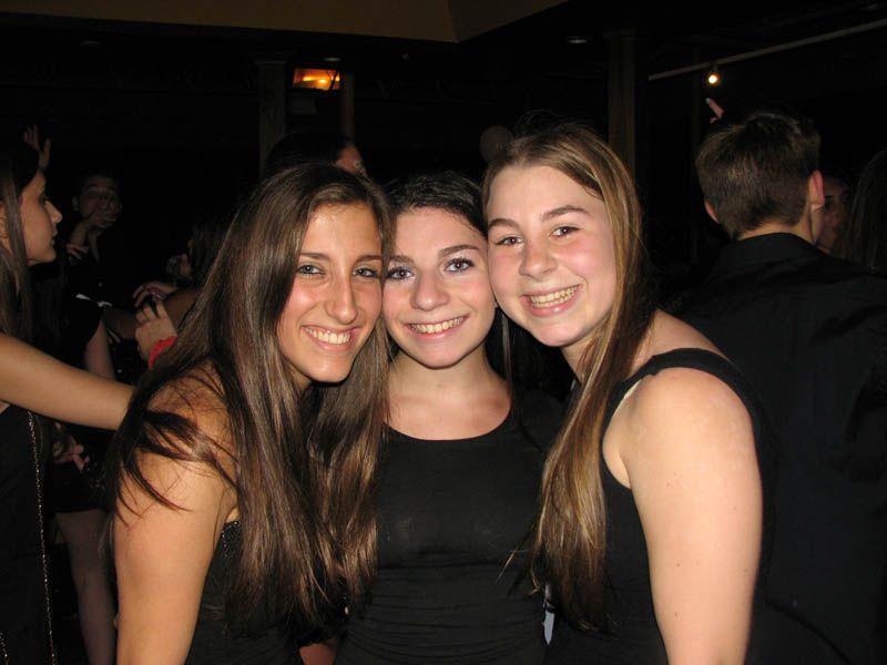Three young people smiling at a dimly lit event.