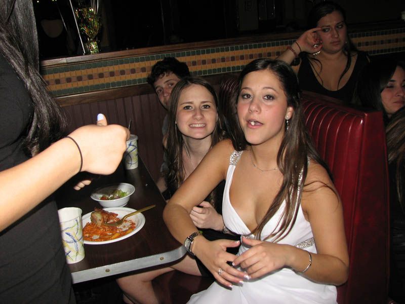 People at a restaurant: one in white dress smiles, others seated in booth, food on table.