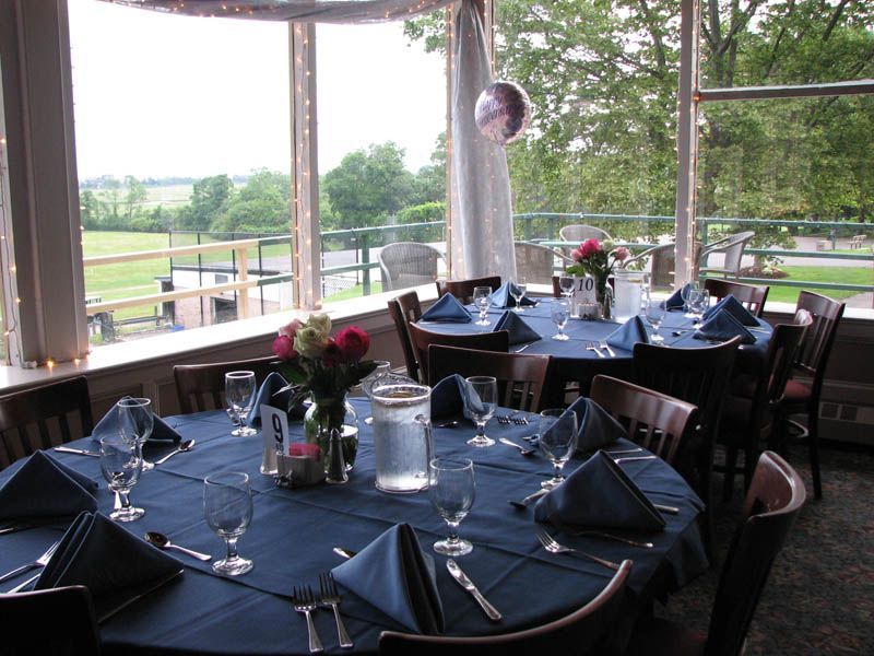 Round tables set for a meal with blue tablecloths, napkins, and floral centerpieces; overlooking a landscape.