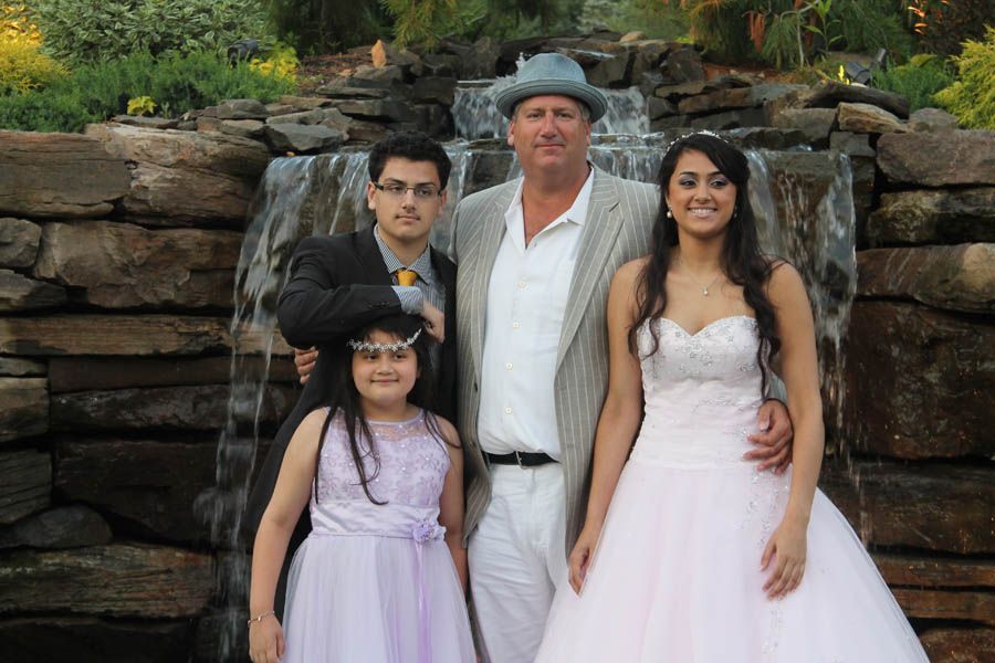 Family posing in front of a waterfall: father in a hat, son in suit, and daughters in formal dresses.