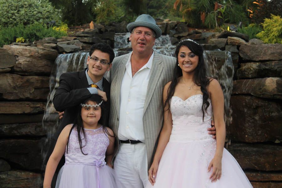 Family posing in front of a waterfall: woman in a white dress, man in a suit jacket, two children in formal wear.