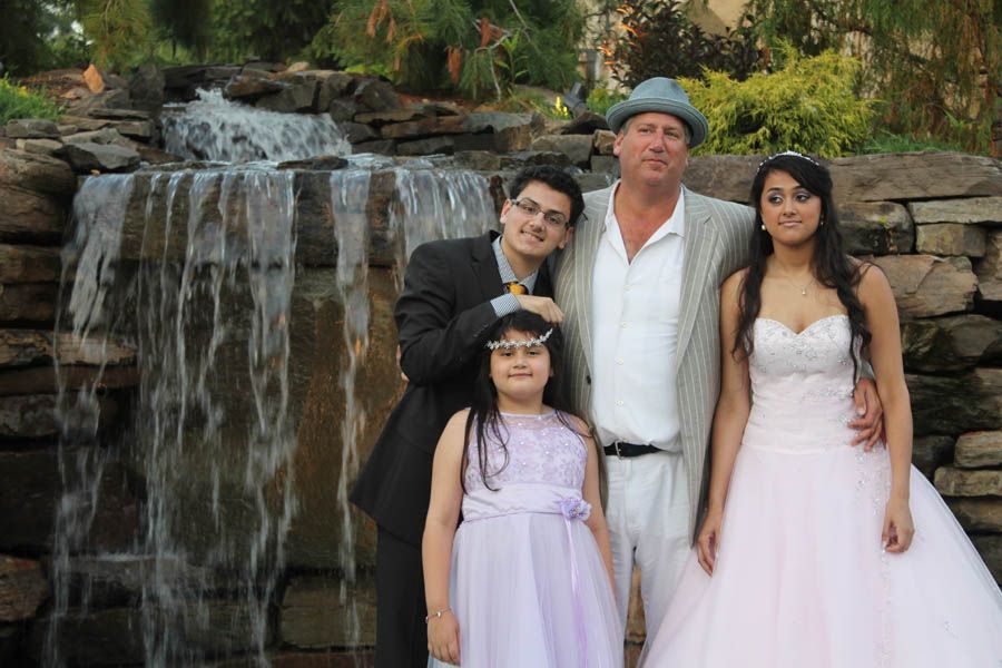 Family of five poses near a waterfall. Formal attire: dresses and suits. Man wears a hat.