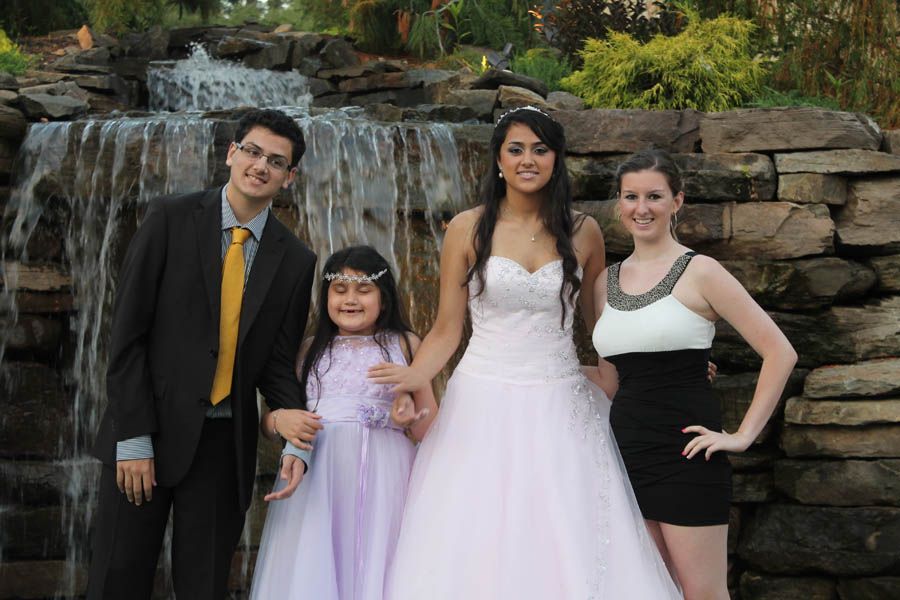 Four people pose in front of a small waterfall: a man, a girl, a woman in a wedding dress, and another woman.