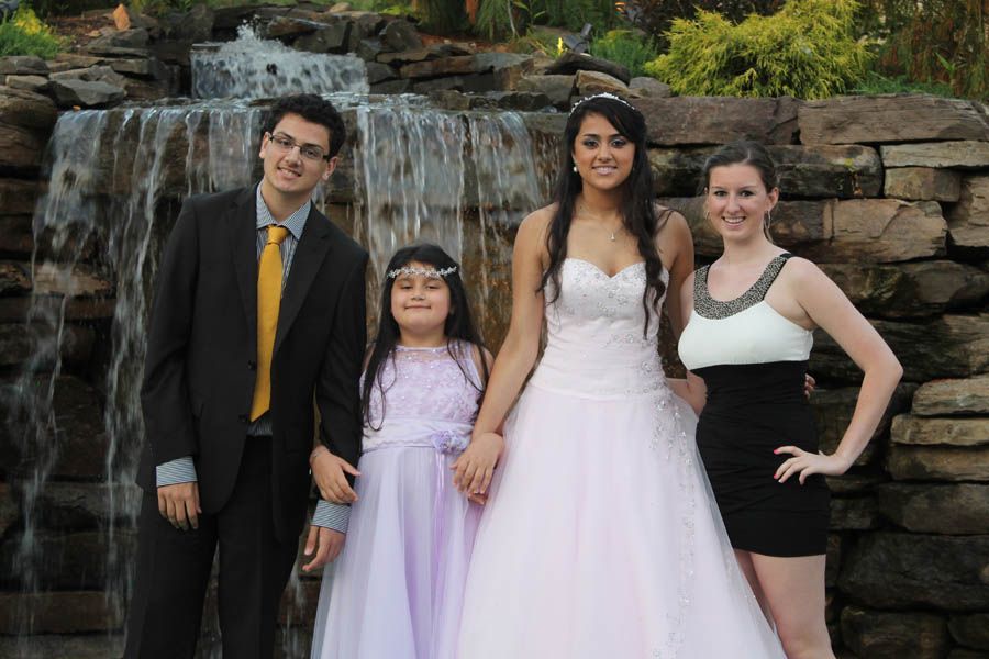Group of four pose in front of waterfall; wedding dress, suit, flower girl dress, and short black dress.
