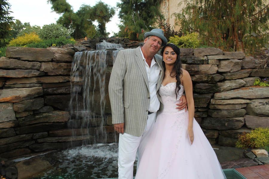 Man in suit and woman in pink dress pose by small waterfall.