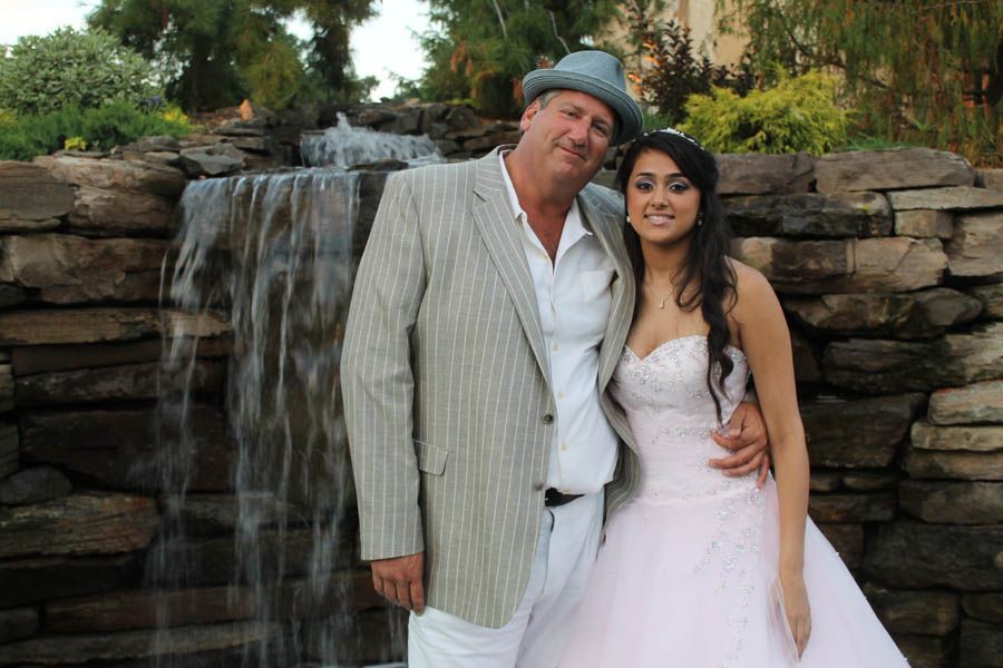 Man in pinstripe suit and woman in pink dress pose by waterfall.