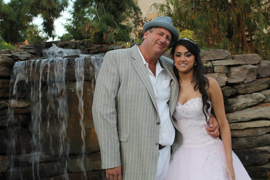 Man in striped suit and woman in pink dress pose by a waterfall.