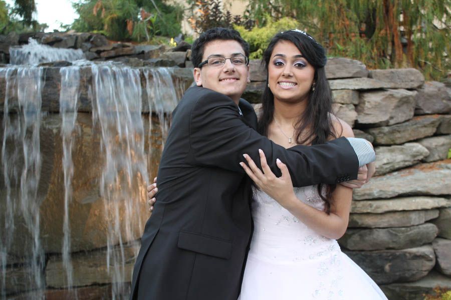 Couple embraces near a waterfall, man in suit, woman in white dress, smiling.