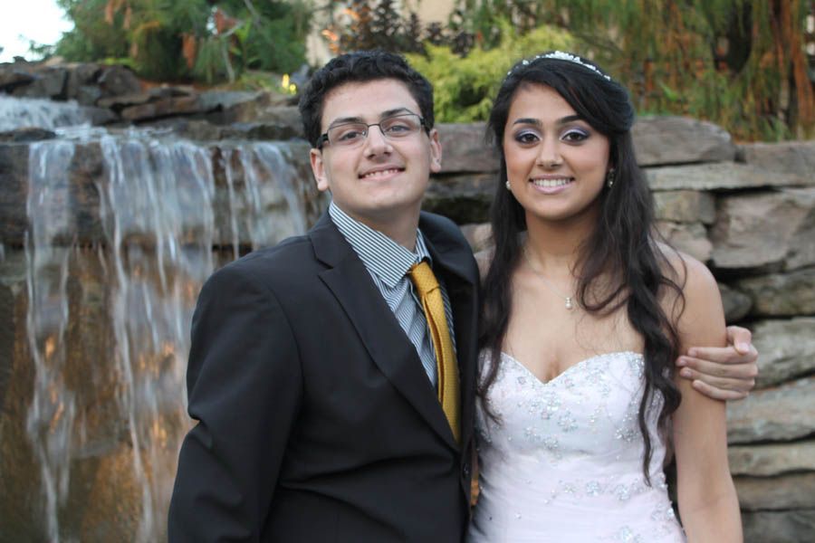Couple poses in front of a waterfall; man wears a suit with a yellow tie, woman in a white strapless dress.