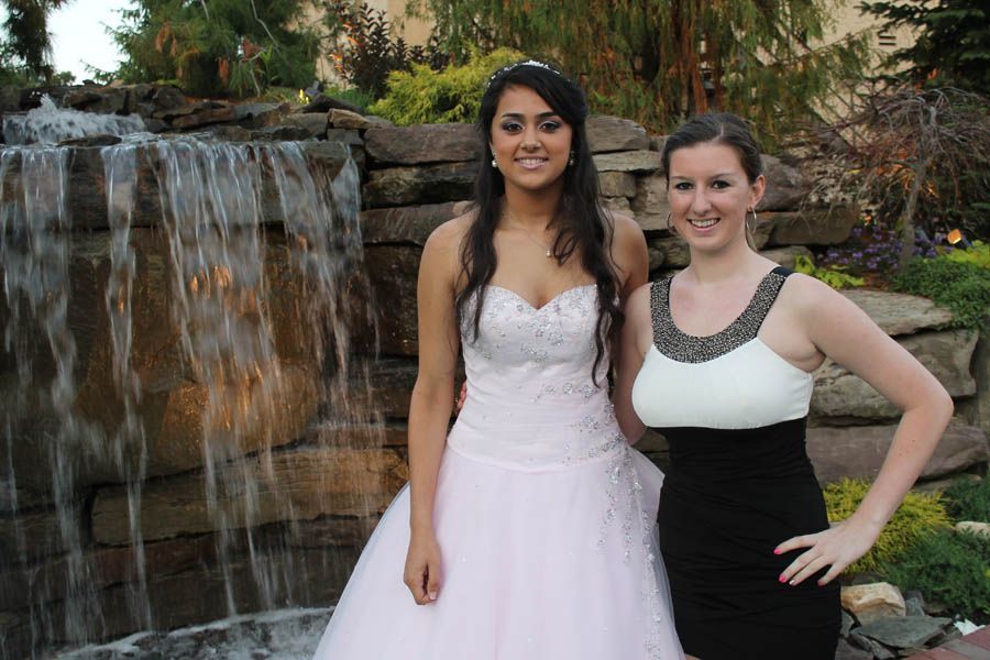 Two women pose by a small waterfall. One wears a white gown, the other a black and white dress.
