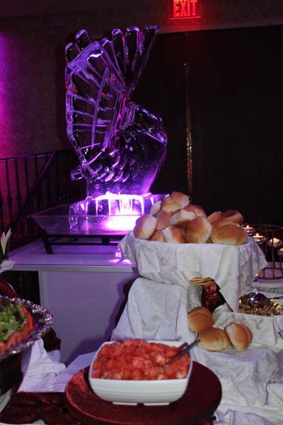 Buffet with ice sculpture centerpiece, food, and rolls. Lit with purple.