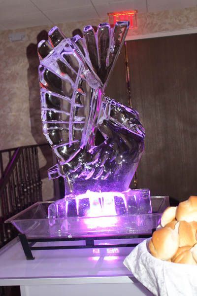 Ice sculpture lit with purple light, atop a serving tray, beside bread rolls.
