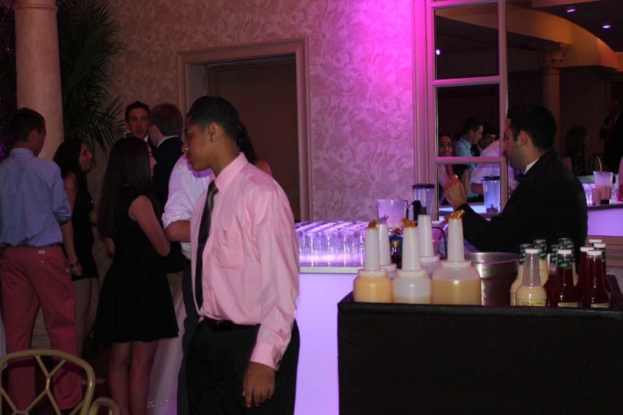 People at a party near a bar. Bartender preparing drinks, pink and white walls.