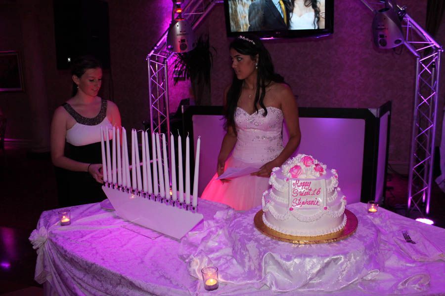 Teenager in gown beside a cake, lit candles, purple lighting, celebration.
