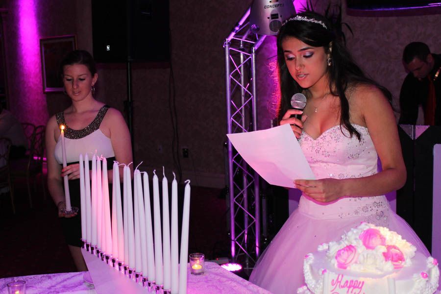 Woman in a formal gown reading into a microphone at a celebration, candles and cake present.