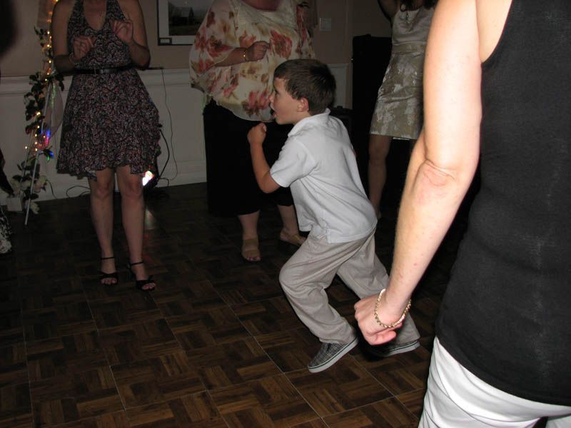 Boy dancing at a party, moving energetically with raised fist and bent knees, surrounded by others.
