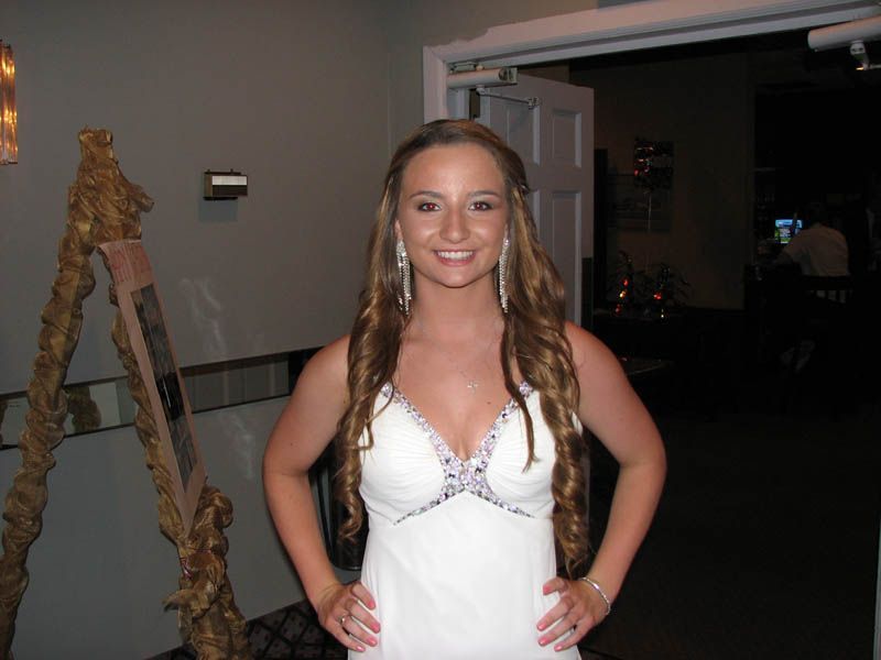 Woman in white formal dress smiles, hands on hips, near an open doorway.