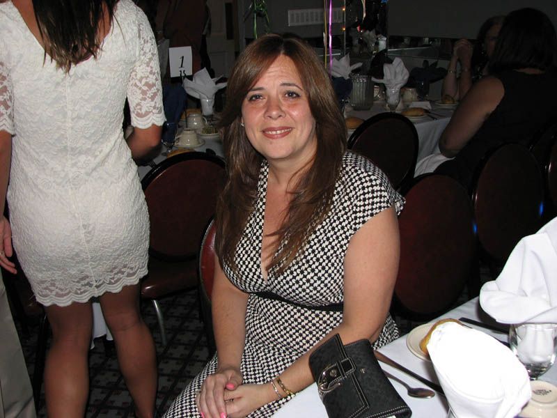 Woman in patterned dress seated at a table, smiling. Dining room setting.