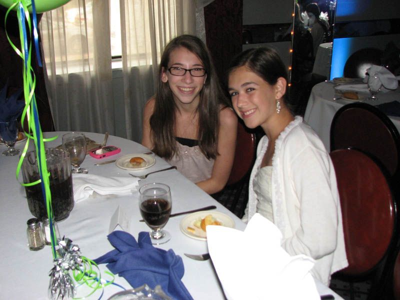 Two smiling girls at a table in a decorated room, balloons visible.