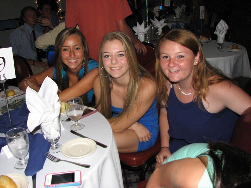 Three young women smiling at a table set for a formal event.