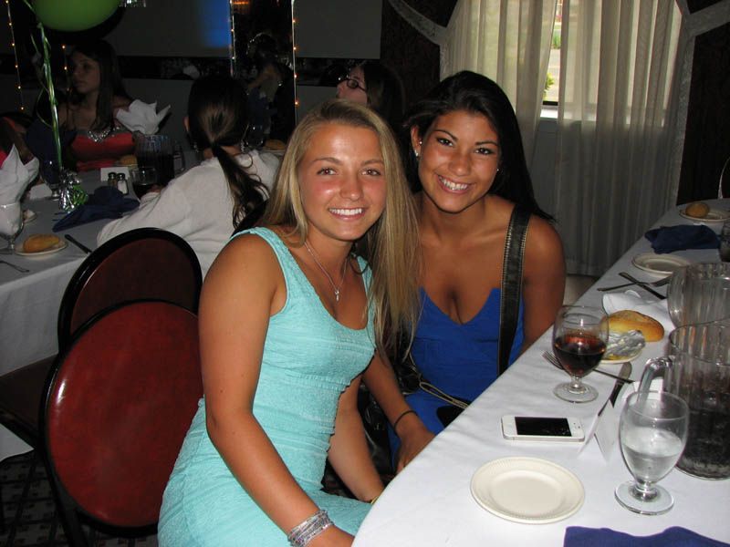 Two women smiling at a table set for a party, one in a blue dress, the other in a turquoise dress.
