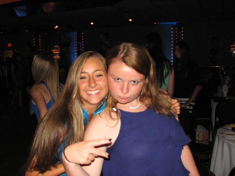 Two young people at a formal event; one smiling, one making a funny face, both in blue dresses.