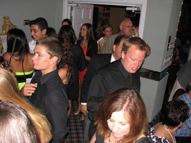 People crowded in a room near an open doorway. Some are wearing black shirts and dresses.