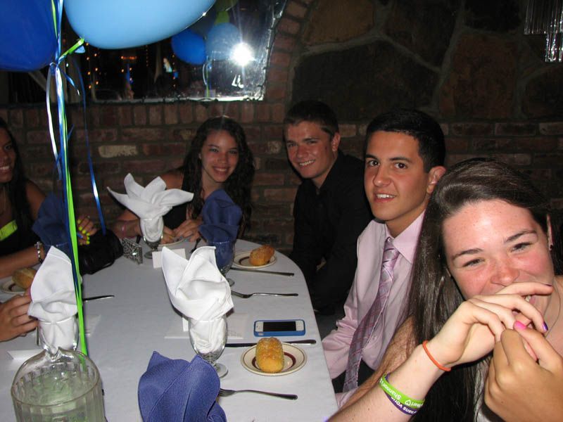 People seated at a table, smiling. Balloons in the background. Restaurant setting with brick wall.