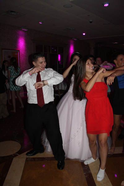 People dancing at an event, a bride in a white dress is in the center; pink lighting.